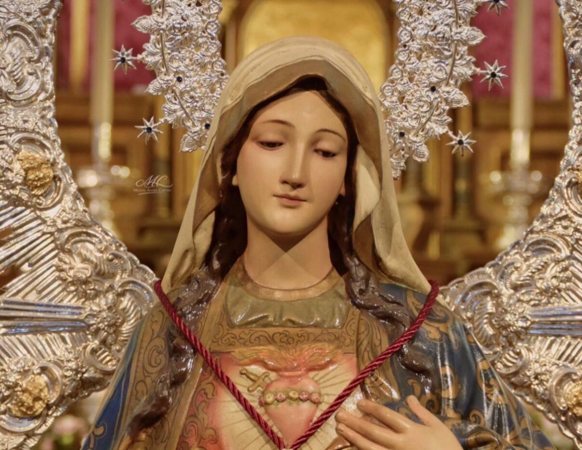 Primer plano de una imagen de la Virgen con manto claro, corazón visible en el pecho y marco de plata calada con estrellas.