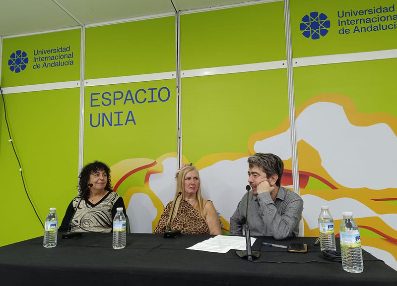 Tres personas sentadas tras una mesa con micrófonos y botellas de agua, ante un panel verde con el texto Espacio UNIA.