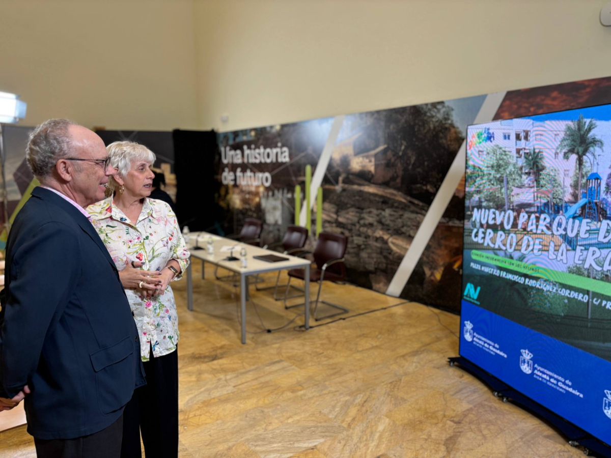 Un hombre y una mujer de pie ante una pantalla que muestra el rótulo Nuevo Parque Cerro de la Era, en una sala con mesa y carteles.