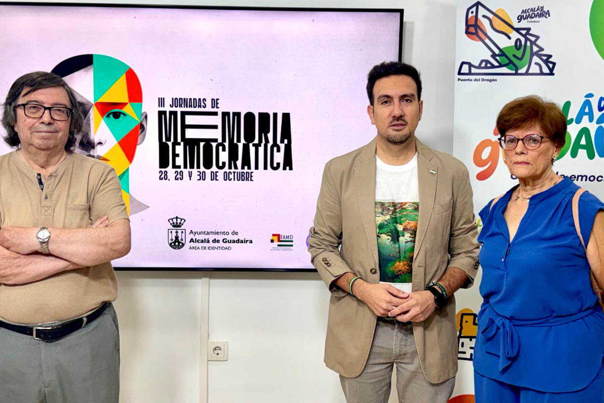 Tres personas de pie posan ante una pantalla que anuncia unas jornadas de memoria democrática.