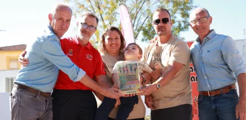 Cinco adultos y un niño sostienen un trofeo con la inscripción XII Carrera Popular Solidaria al aire libre.