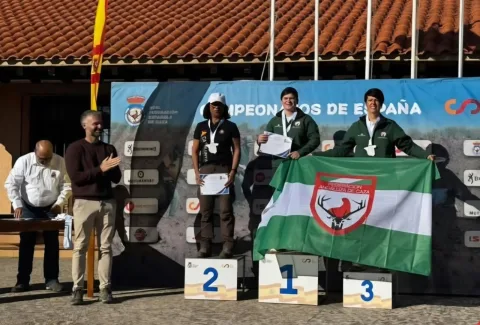 Tres deportistas con medallas y diplomas posan en un podio ante un cartel de campeonatos de España, una con bandera verde y blanca.