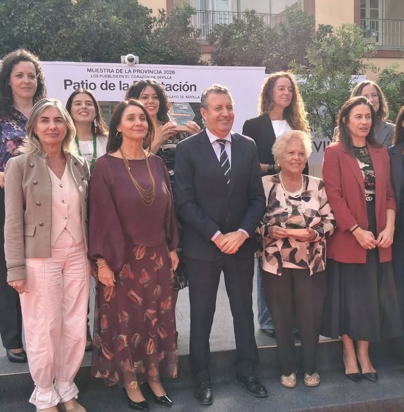 Un grupo de personas posa sonriente ante una pancarta sobre un patio, con un hombre trajeado en el centro.