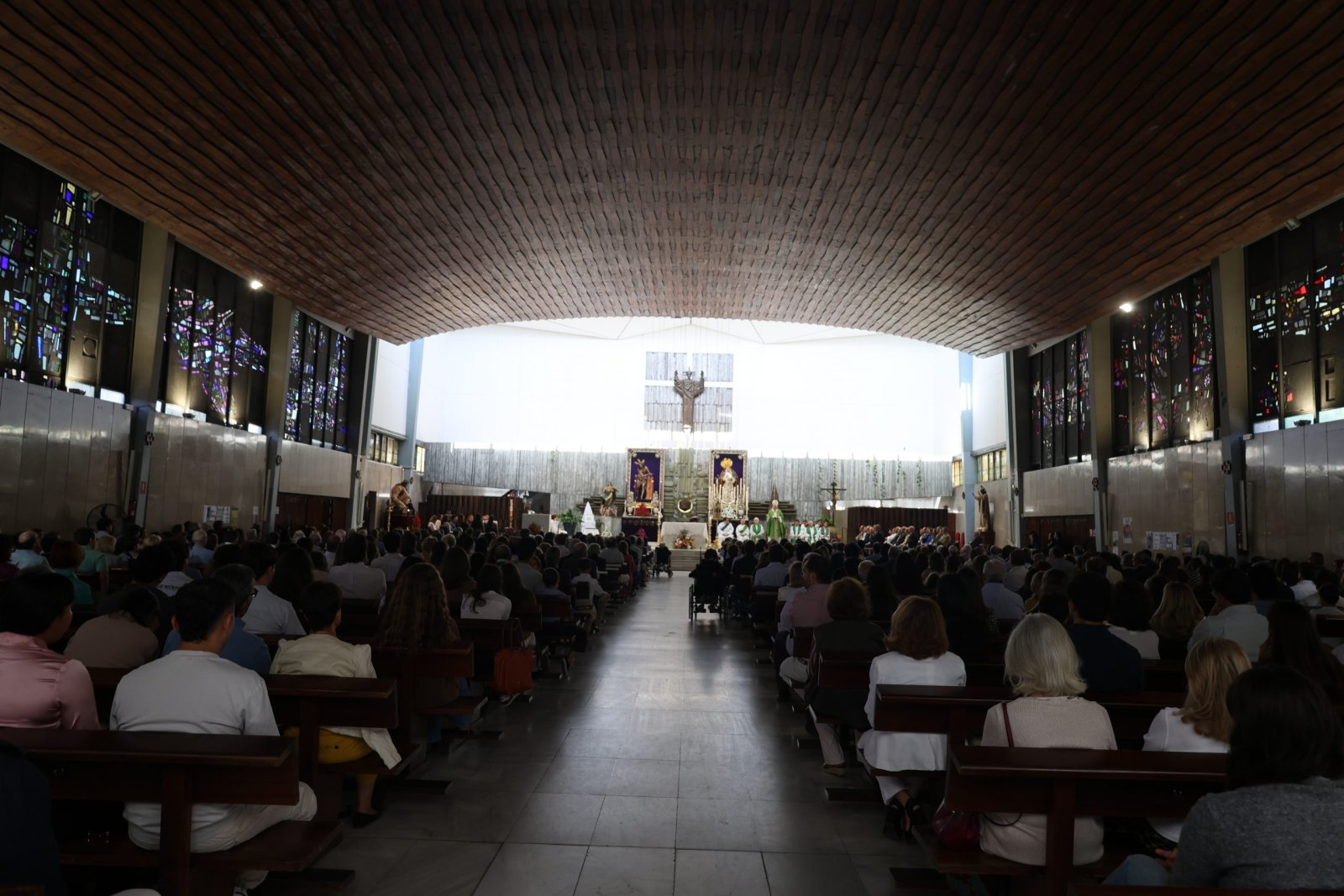 Interior de una iglesia llena de fieles sentados en bancos, con el altar y un retablo al fondo.