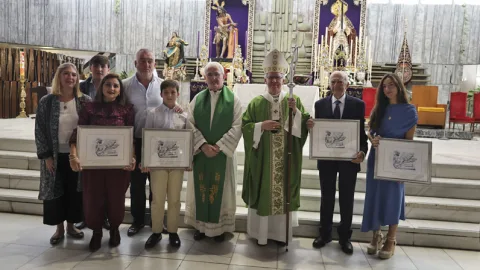 Un grupo de personas posa en el presbiterio de una iglesia junto a dos sacerdotes, con diplomas enmarcados y retablos al fondo.