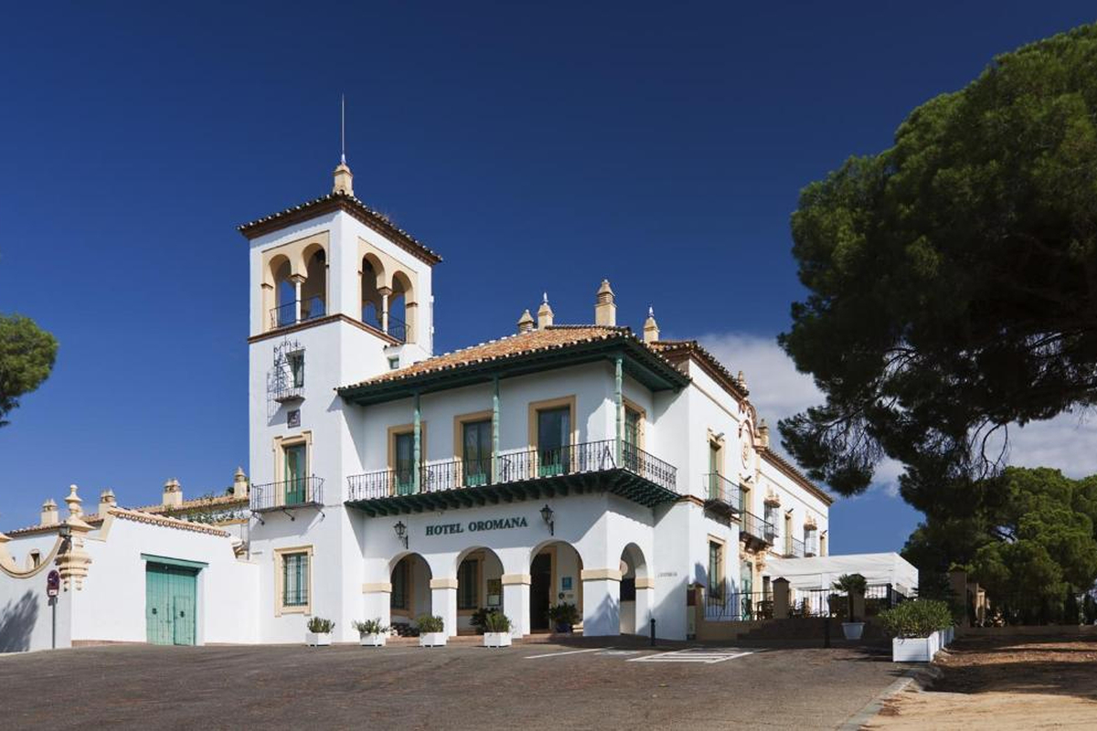 Edificio blanco de estilo regionalista con torre y arcos, rótulo Hotel Oromana, junto a grandes pinos.