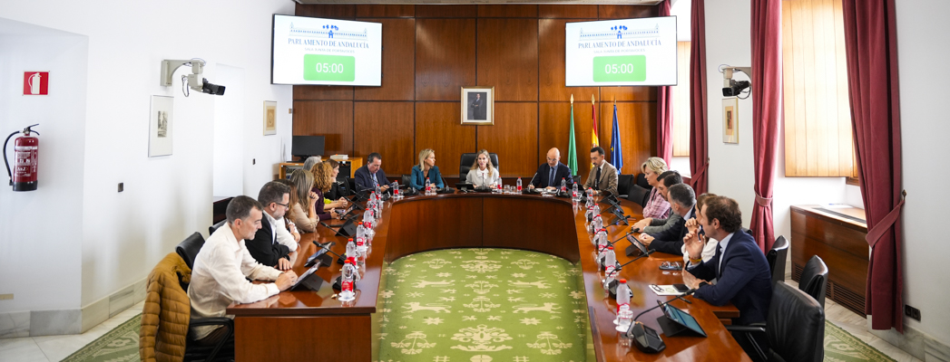 Varias personas sentadas alrededor de una mesa ovalada en una sala de reuniones con pantallas que marcan 05:00.