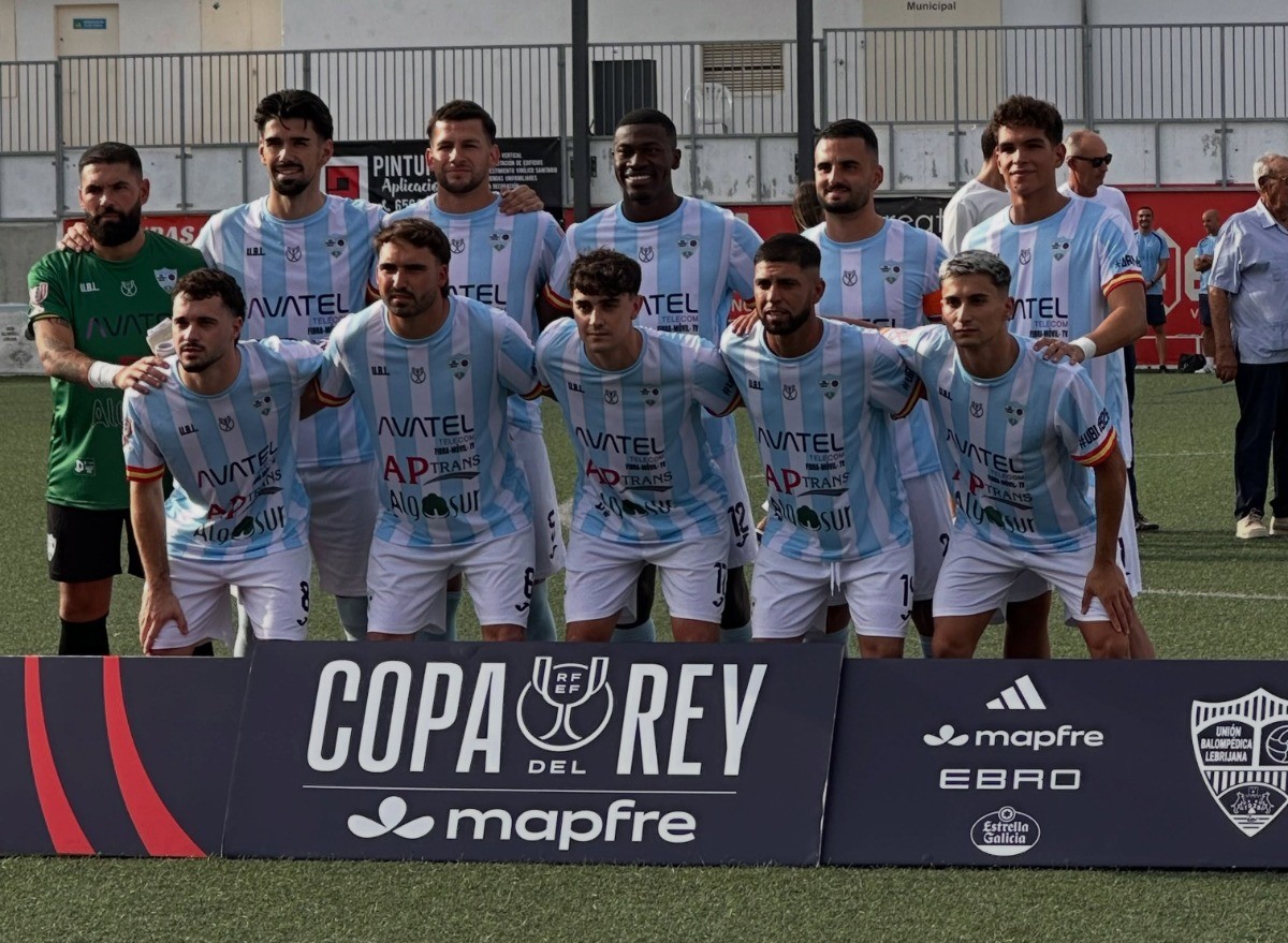 Un equipo de fútbol con camisetas azul celeste y blanca posa en fila sobre el césped detrás de un cartel de la Copa del Rey.