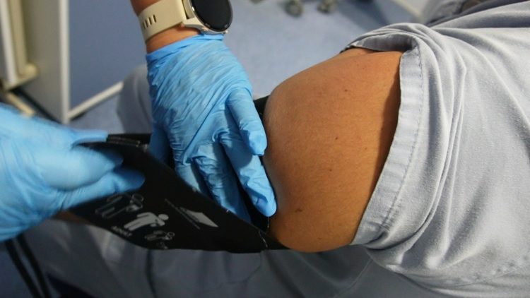 Manos con guantes azules colocan un manguito de tensión en el brazo de una persona.