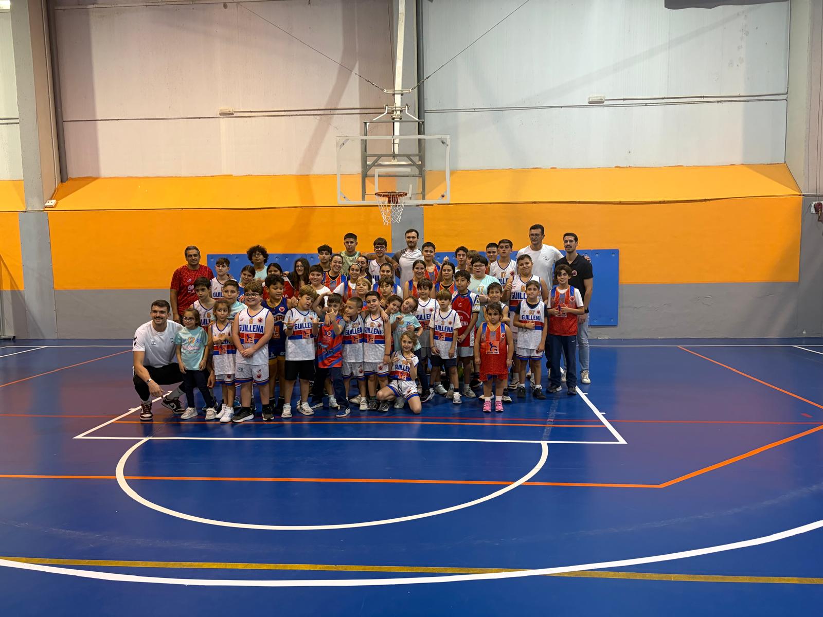 Grupo de niños y adultos con equipaciones deportivas posando en una cancha cubierta de baloncesto.