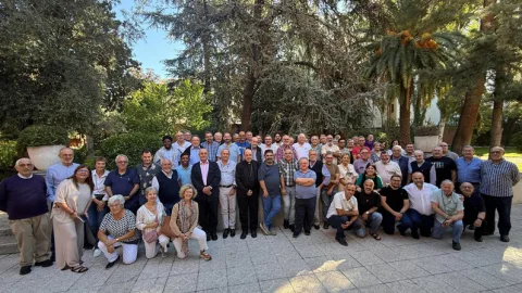 Un grupo numeroso de personas posa al aire libre en una plaza ajardinada con árboles y palmeras.