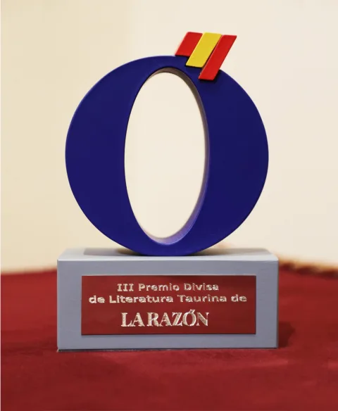Trofeo con un aro azul y franjas roja y amarilla sobre una base gris con placa roja del III Premio Divisa de Literatura Taurina.