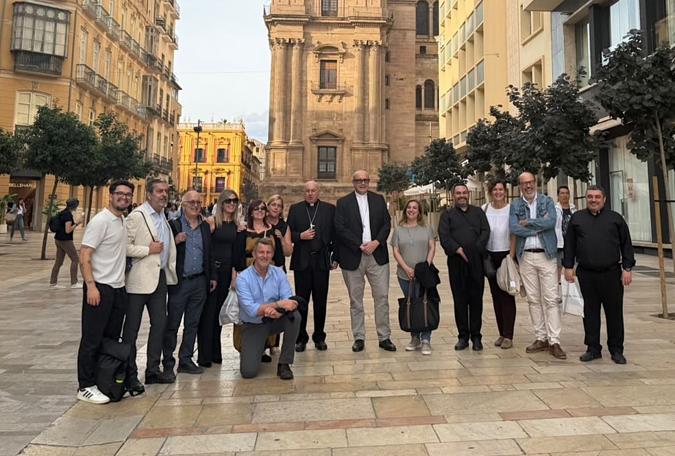 Un grupo de unas quince personas posa en una plaza empedrada, con una gran iglesia de piedra al fondo y edificios alrededor.