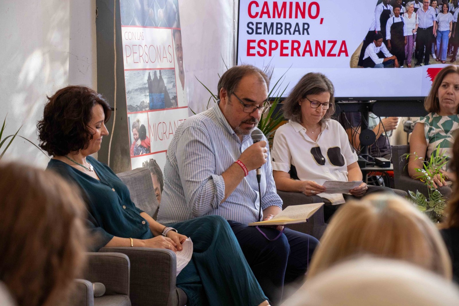 Un hombre con gafas habla por un micrófono sentado entre dos mujeres, ante un cartel que dice Camino, sembrar esperanza.