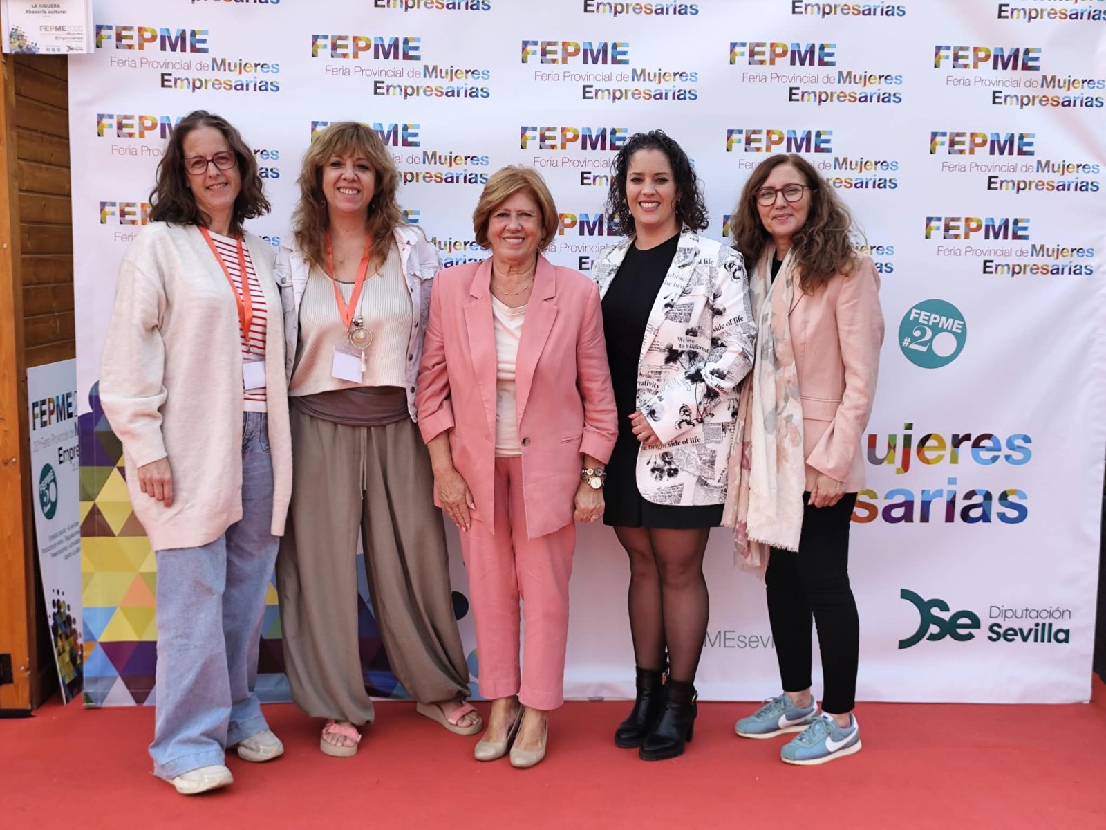 Cinco mujeres de pie y sonrientes sobre una alfombra roja ante un panel con el texto FEPME, Feria Provincial de Mujeres Empresarias.