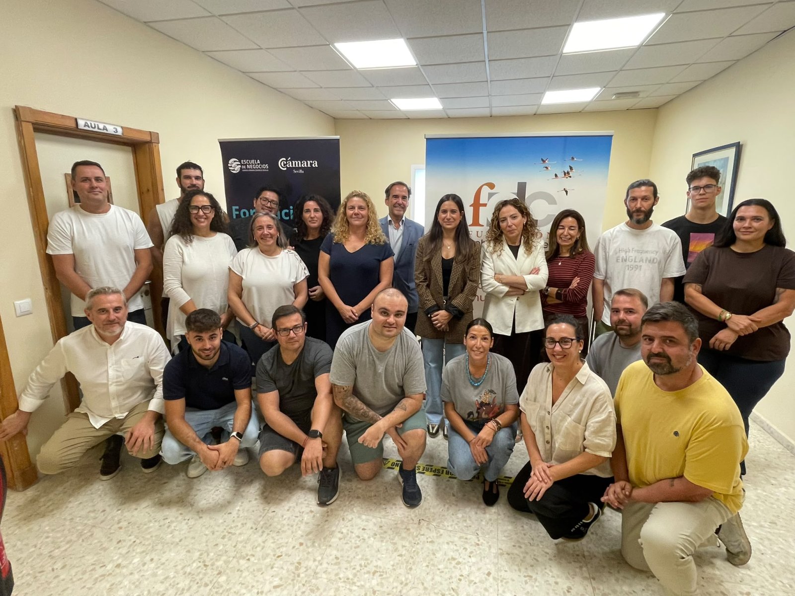 Un grupo de unas veinte personas posa en una sala con carteles de la Escuela de Negocios y la Cámara de Sevilla, junto a una puerta rotulada Aula 3.