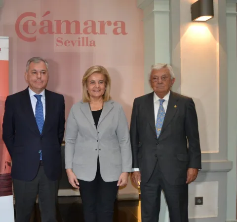 Tres personas trajeadas posan ante un panel rosa con el texto Cámara Sevilla.