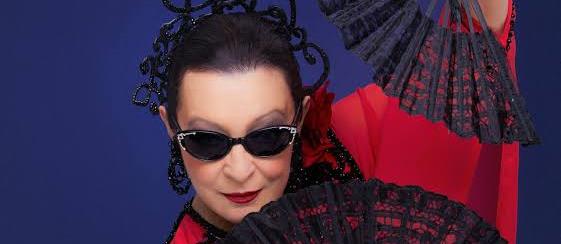 Mujer con gafas de sol, tocado de rejilla negro y vestido rojo, sosteniendo abanicos negros calados sobre fondo azul.